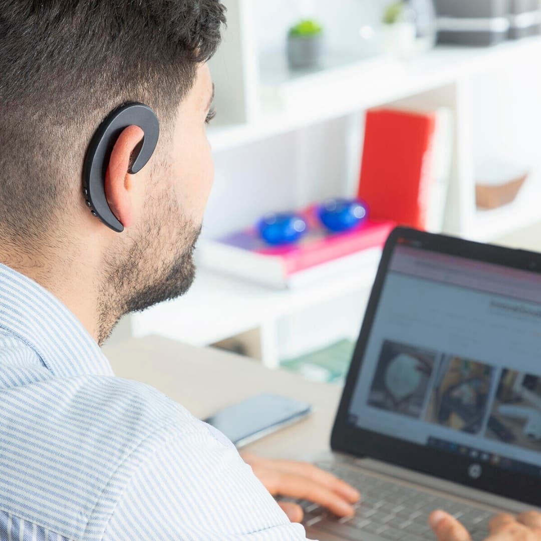 Auricular open-ear utilizado en oficina permitiendo escuchar entorno y llamadas
