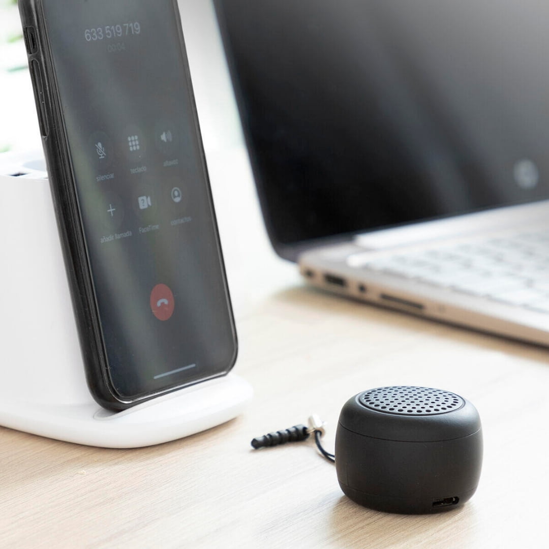 Mini altavoz portátil colocado en escritorio junto a smartphone durante llamada manos libres