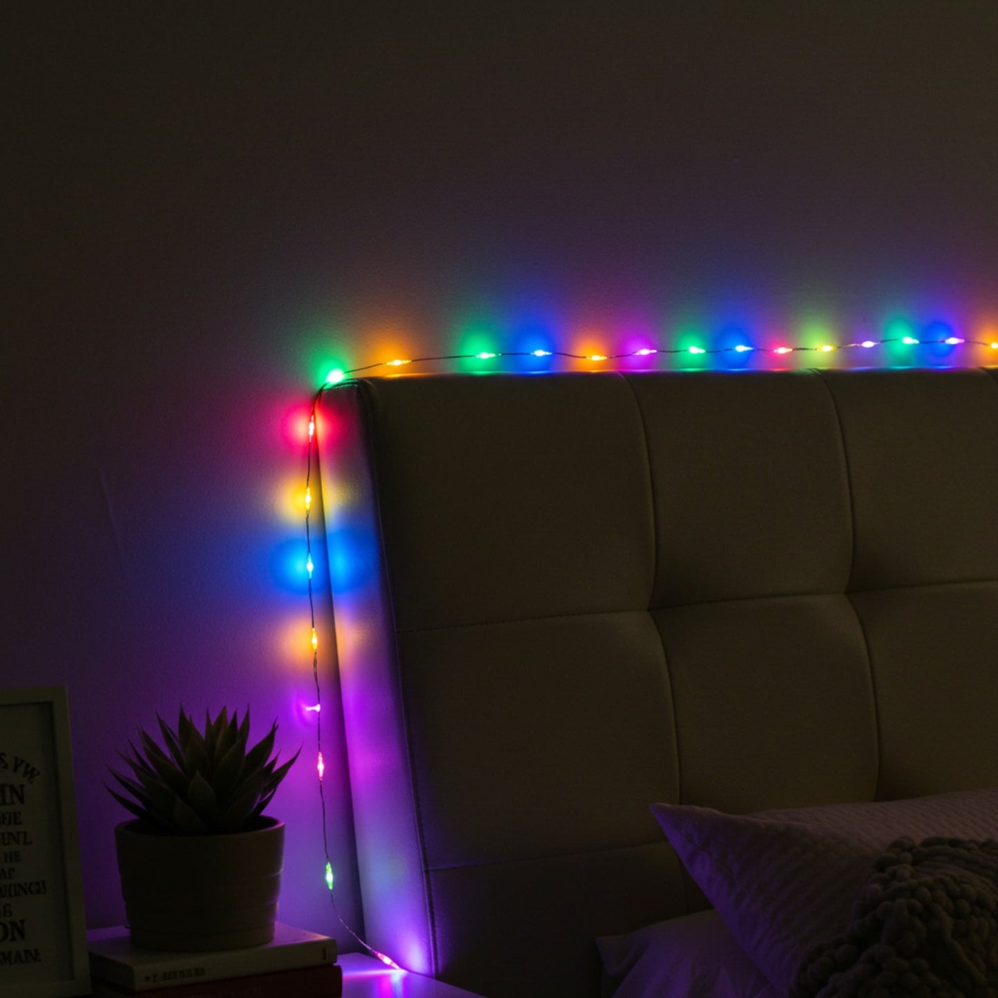 Guirnalda de luces multicolor decorando cabecera de cama, creando ambiente cálido y moderno.