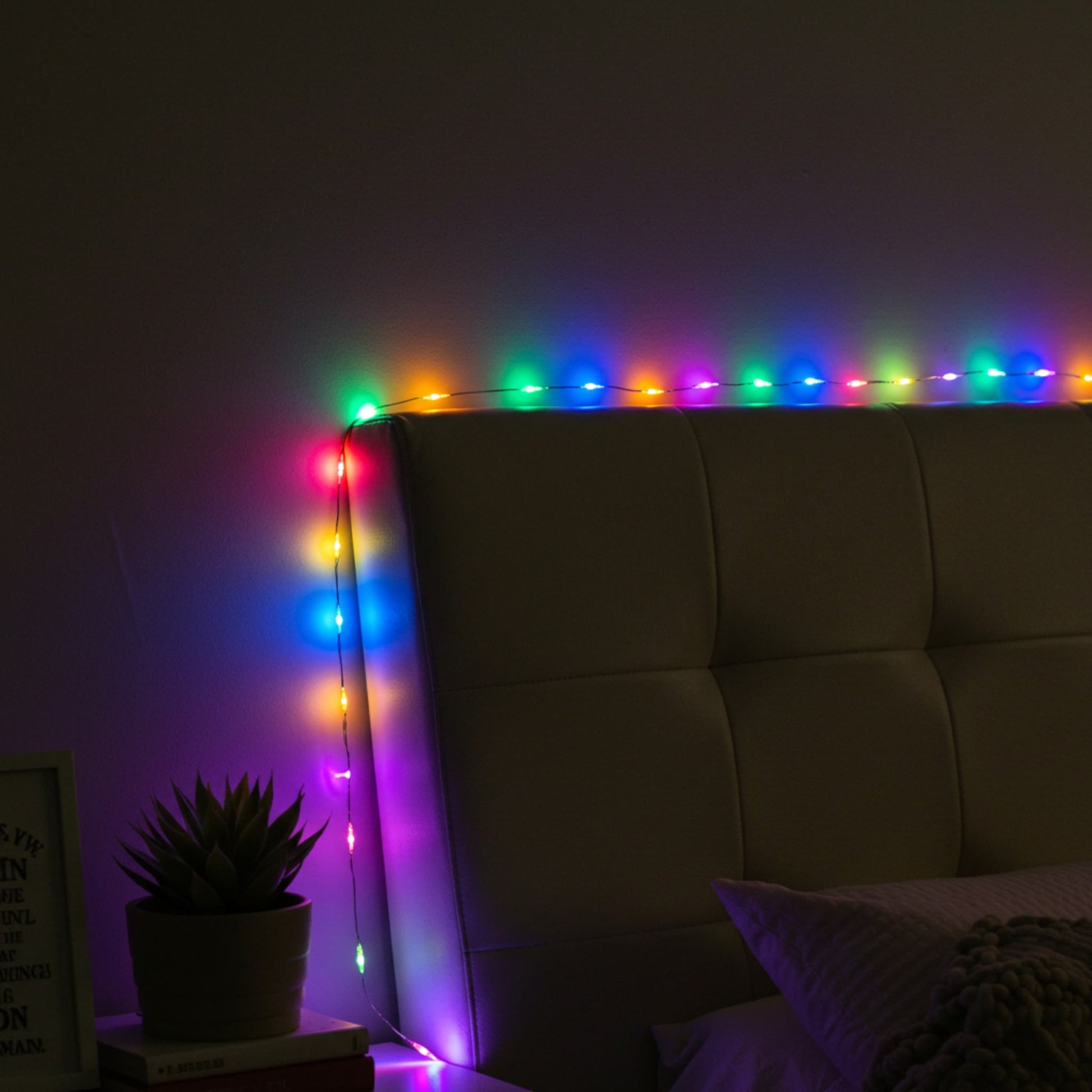 Guirnalda de luces multicolor decorando cabecera de cama, creando ambiente cálido y moderno.