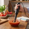 Batidora de mano Kiwi negra triturando salsa de tomate en un bol de cristal. Demostración de potencia para texturas homogéneas y sin grumos.