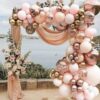 Globos oro rosa y dorado decorando una celebración en la playa con fondo de mar y arena