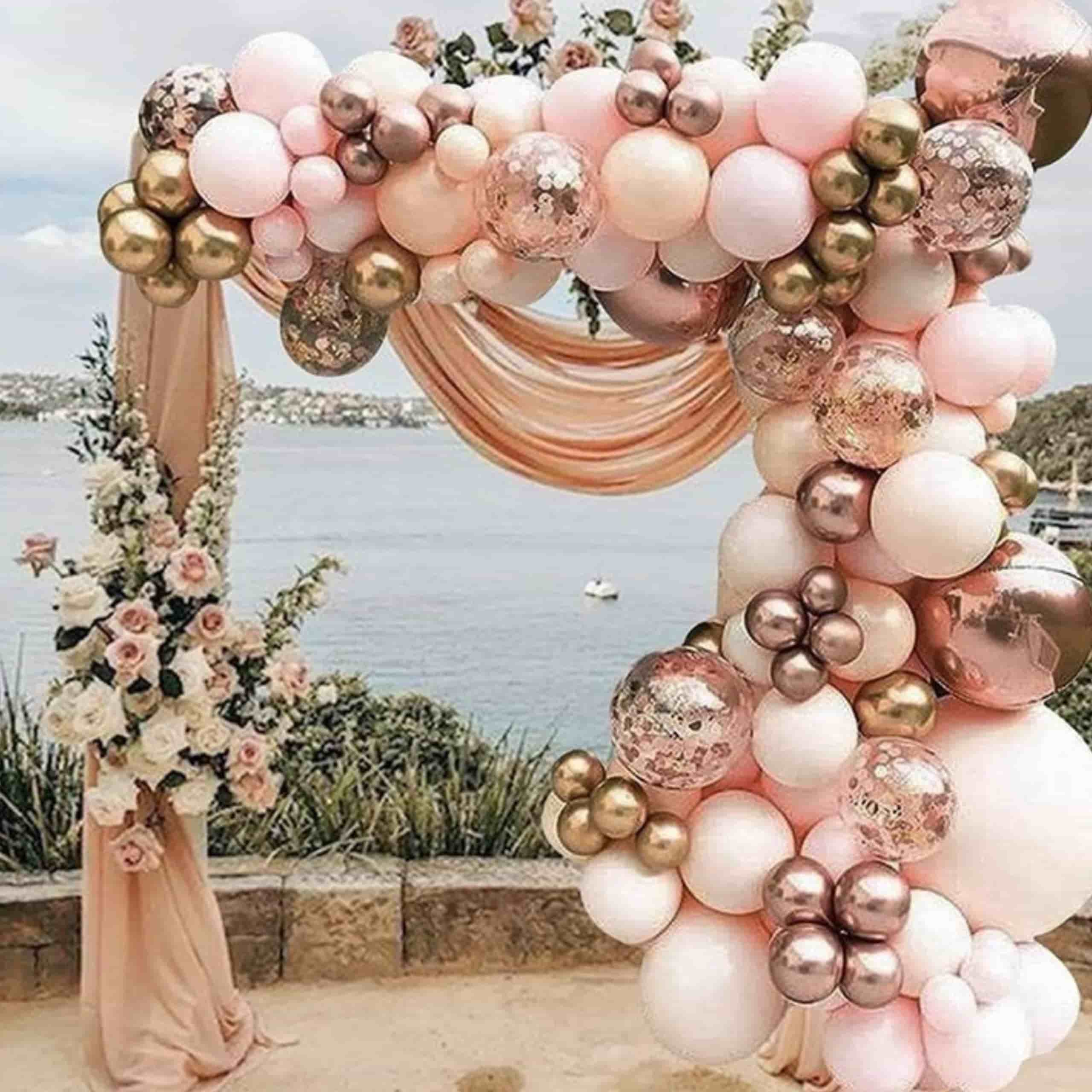 Globos oro rosa y dorado decorando una celebración en la playa con fondo de mar y arena