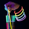 Pulseras fluorescentes Lumi Flex en uso con vaso luminoso Mano sosteniendo un vaso iluminado decorado con pulseras fluorescentes Lumi Flex en una fiesta nocturna