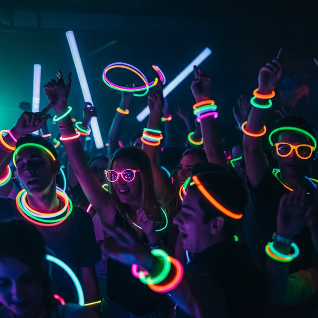 Jóvenes en concierto usando pulseras luminosas Opti Glow multicolor durante una fiesta nocturna