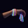 Mano con pulseras luminosas GlowMaster Pro encendidas Mano mostrando pulseras luminosas GlowMaster Pro encendidas con colores intensos en ambiente oscuro