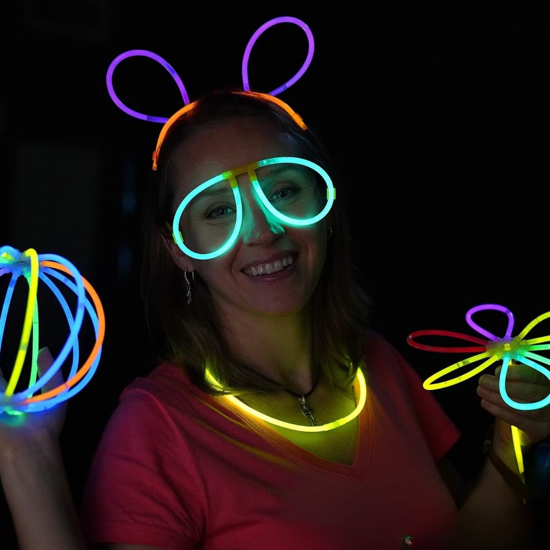 Chica usando pulseras fluorescentes Opti Glow como collares, gafas y accesorios luminosos en una fiesta