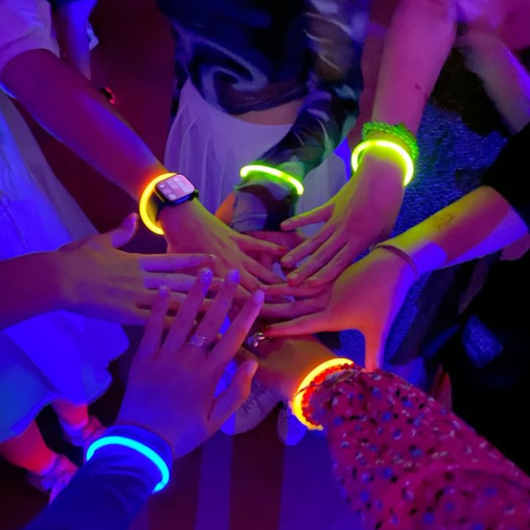 Manos con pulseras luminosas Glow Elite encendidas Manos juntas con pulseras luminosas Glow Elite encendidas mostrando colores intensos en la oscuridad