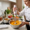 Triturando cremas suaves con batidora de brazo Chef utilizando batidora de mano para triturar una crema de verduras naranja en un bol de acero inoxidable.