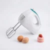 Batidora de mano eléctrica blanca de 200W junto a huevos y un postre de fresa sobre fondo blanco.