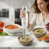 Cómo hacer purés y cremas sin grumos Mujer utilizando la batidora de mano Kiwi para batir una crema de champiñones en un bol sobre encimera de mármol.