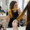 Aplicación fácil del spray de color en casa Mujer aplicando spray de color oro en las puntas del cabello frente al espejo con guantes para un retoque de color rápido.