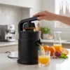 Mujer utilizando un exprimidor de palanca eléctrico en una cocina moderna para preparar zumo de naranja natural recién exprimido.