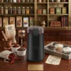 Molinillo de café integrado en una decoración de cocina con una prensa francesa y bolsas de café de origen, ideal para molienda fresca diaria.