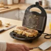 Dos sándwiches tipo panini cocinándose uniformemente en las placas antiadherentes de 750W de la sandwichera eléctrica DVTech.