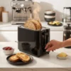 Tostadora para Pan Rústico y Rebanadas Gruesas Tostadora moderna de color negro en una cocina minimalista junto a un desayuno saludable, ideal para tostar pan de pueblo y rebanadas anchas.