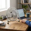 Primer plano de un ventilador de mesa DV TECH de metal junto a una laptop y café, mostrando su tamaño compacto y diseño industrial.