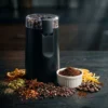 Molinillo eléctrico multifunción rodeado de pimienta, canela, cardamomo y granos de café, demostrando su versatilidad para condimentos.