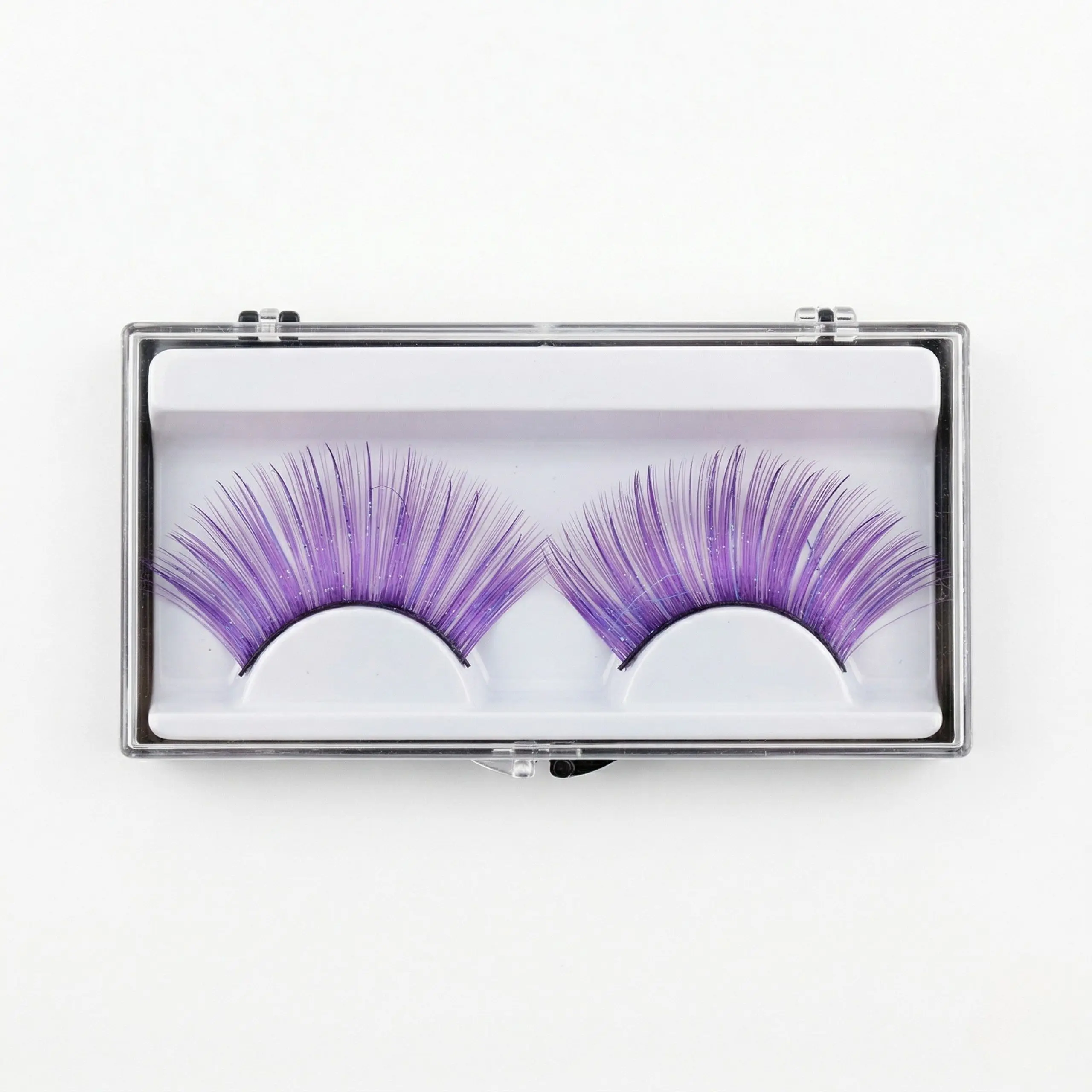 Pestañas Postizas Violetas con Brillo – Vista Frontal Pestañas postizas moradas de fantasía con glitter en estuche transparente sobre fondo blanco profesional.