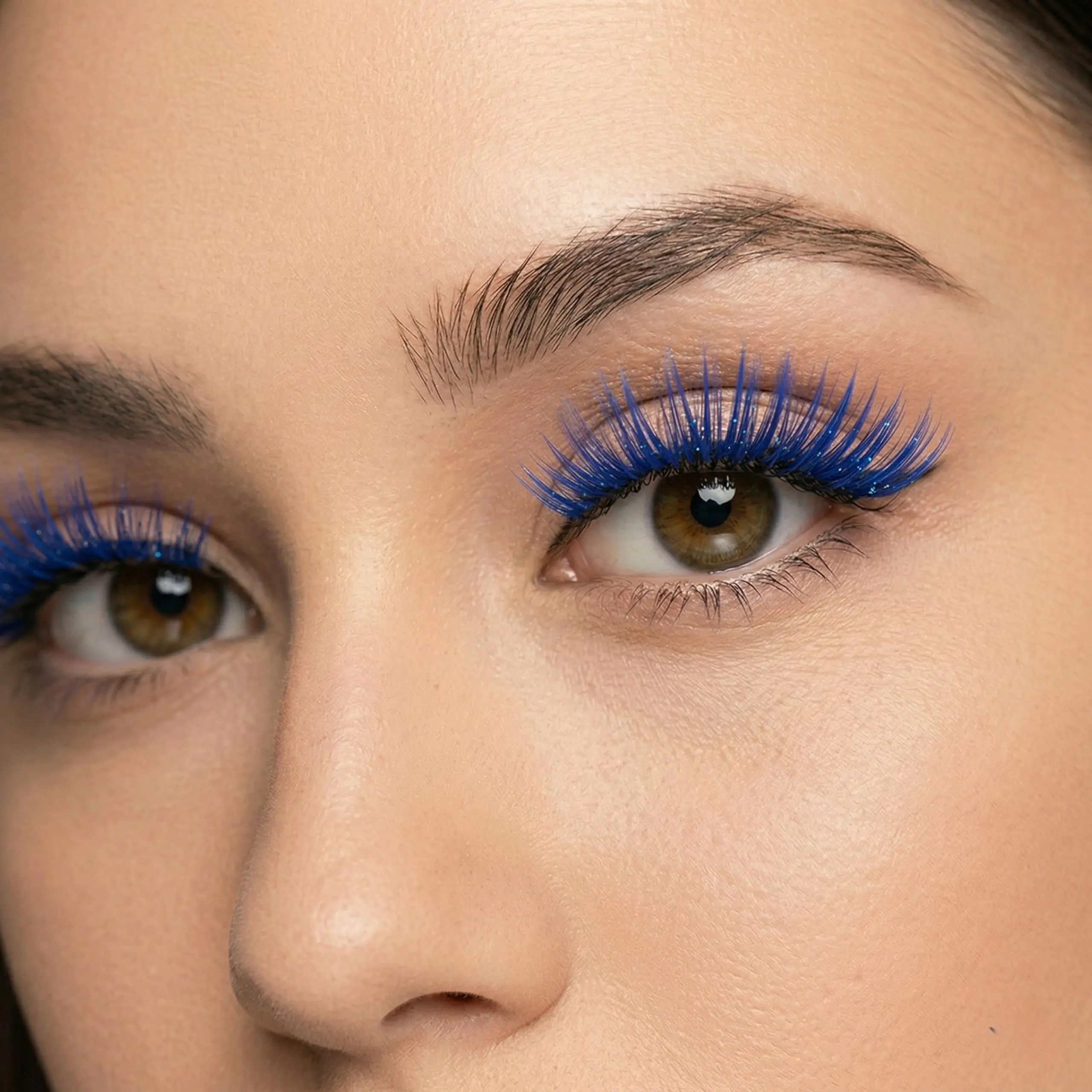 Volumen y Longitud Azul Eléctrico Primer plano en ángulo de tres cuartos del ojo marrón de una mujer, mostrando la longitud, volumen y textura con purpurina de las pestañas postizas azules.