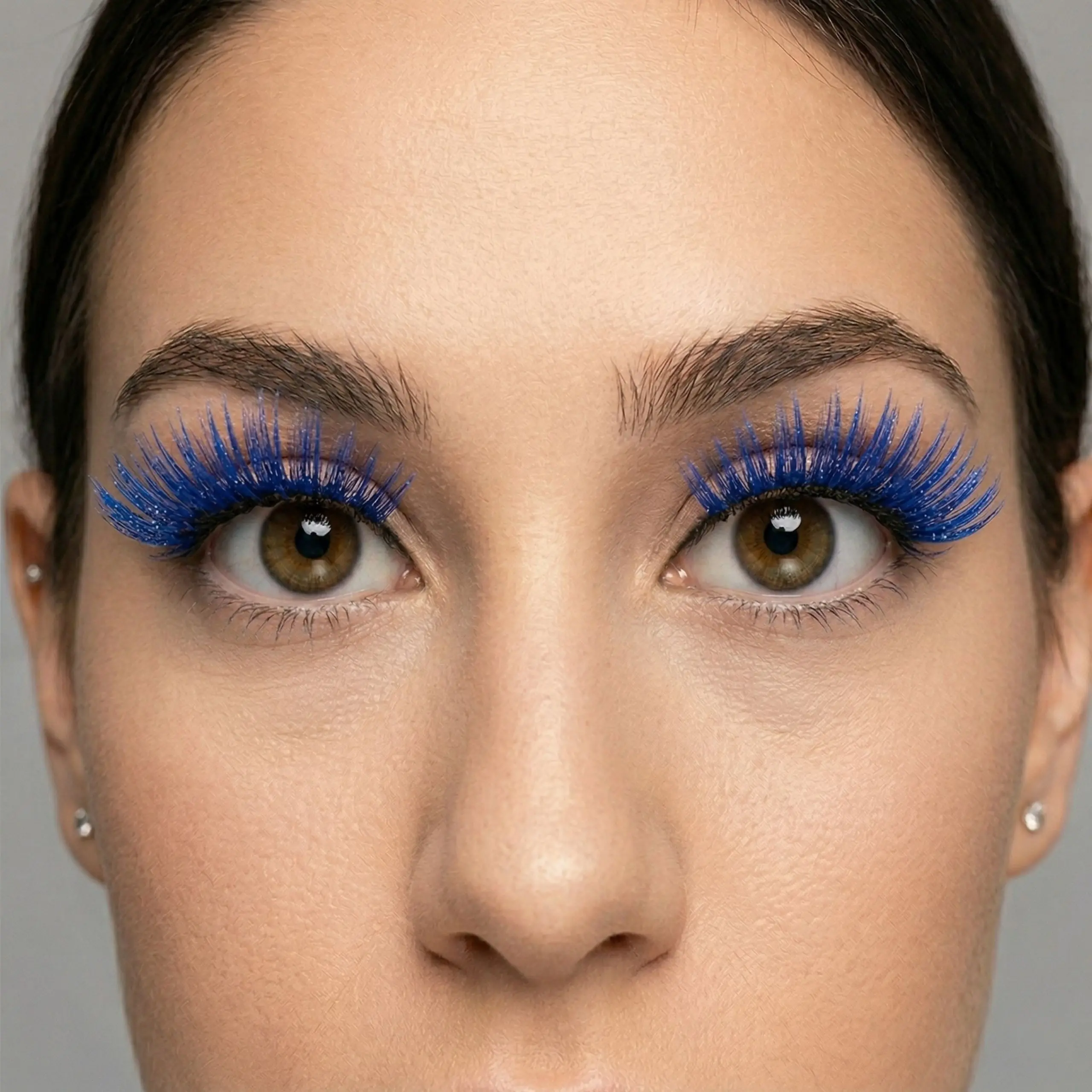 Mirada Impactante en Azul Primer plano frontal de los ojos marrones de una mujer usando pestañas postizas tupidas y largas de color azul eléctrico vibrante con purpurina.