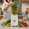 Preparación de Batidos Verdes con Vita-Blend Persona preparando un batido verde detox con espinacas, brócoli y zanahoria en una licuadora individual de vaso.