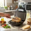 Mano retirando un panini crujiente con queso derretido de una sandwichera grill DVTech con placas antiadherentes estriadas.