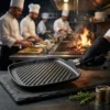 Chef profesional utilizando una sartén grill de aluminio fundido en una cocina de alto rendimiento para sellar carnes.