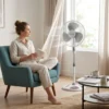 Confort en el Hogar Mujer relajada leyendo en un sillón con el ventilador de pie DVTECH funcionando de forma silenciosa en la sala de estar.