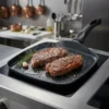 Filetes de carne cocinándose en asadora lisa de aluminio sobre placa de inducción para una cocción uniforme.