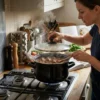 Mujer cocinando un guiso con tapa en una olla esmaltada negra en estufa
